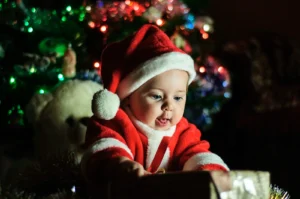 Bébé en tenue de Père Noël devant un sapin illuminé, premier Noël